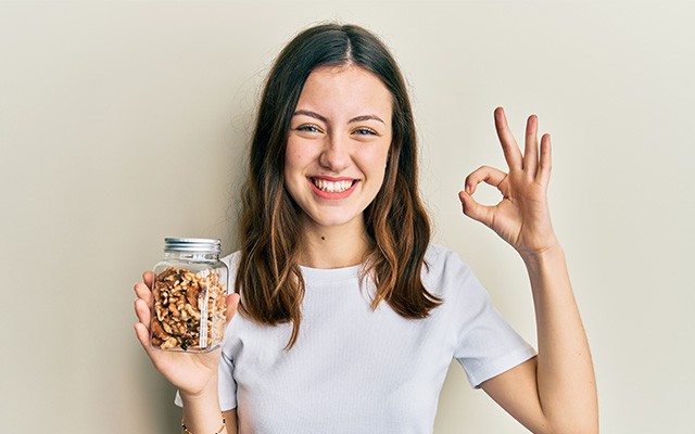 Lächelnde junge Dame hält ein Glas mit Walnüsse mit der rechten Hand hoch